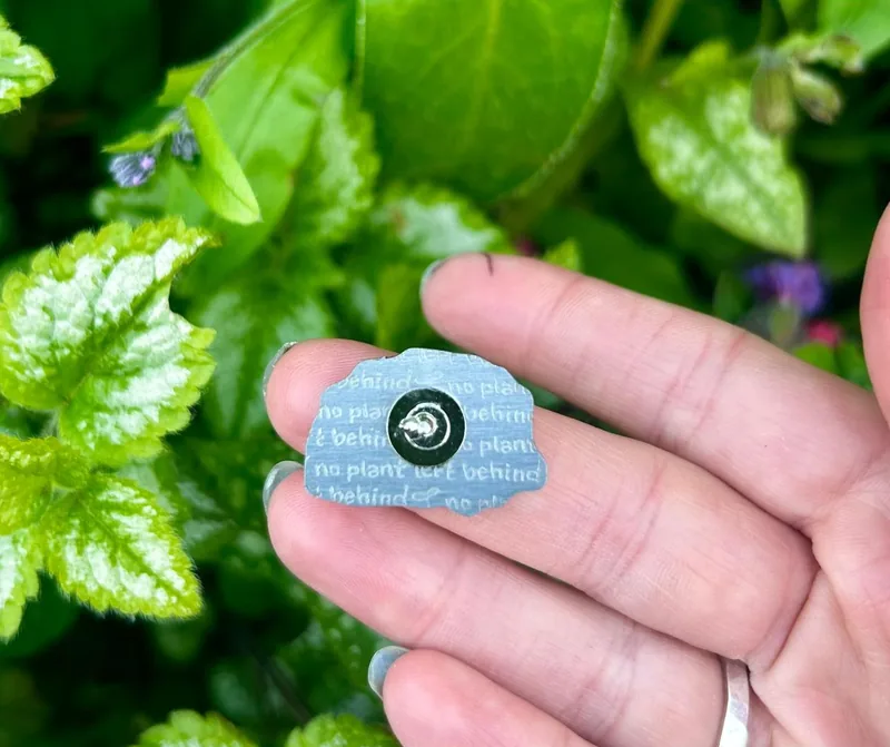 The back of a pin, stamped with No Plant Left Behind